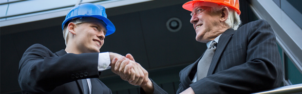 Two smiling men in suits, wearing hard hats, shaking hands